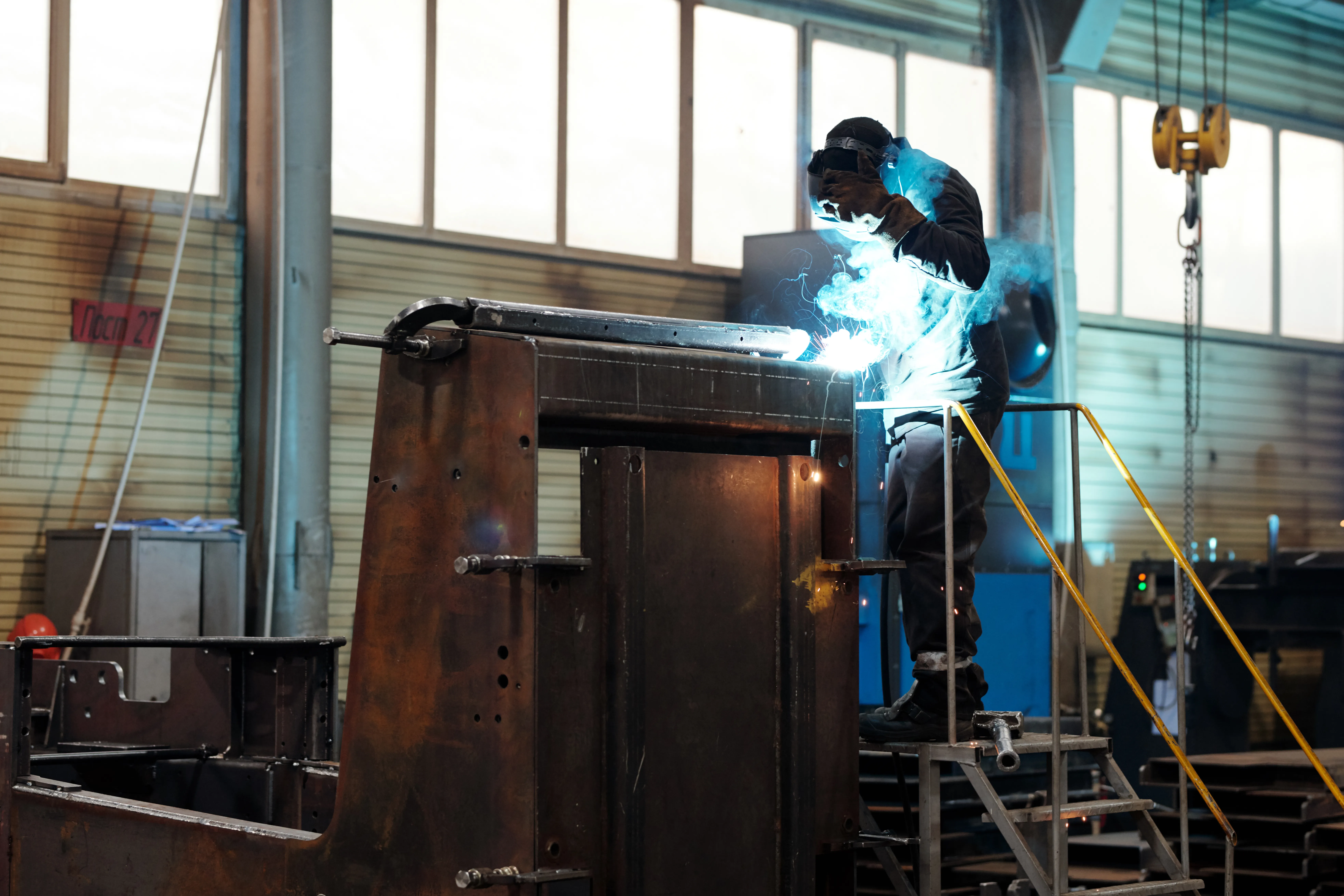 Image of man welding a complex piece of engineering and factory equipment while wearing PPE.